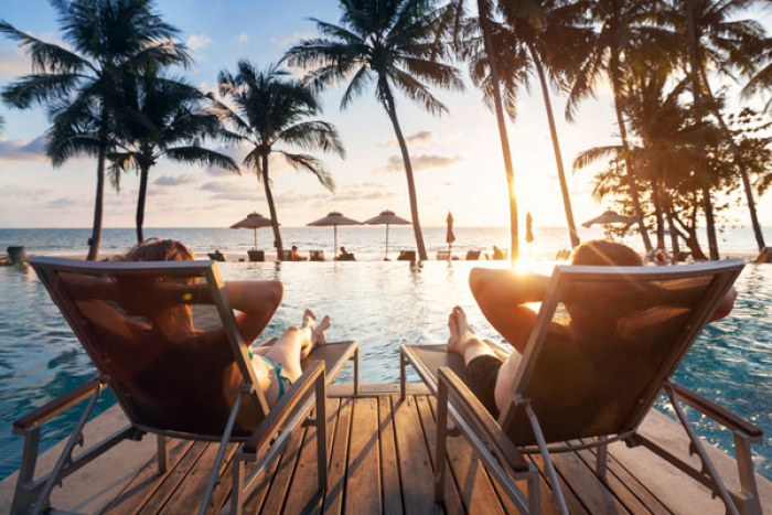 Couple sitting on deck chairs facing ocean at sunset