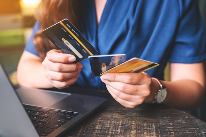 woman holding three credit cards in front of laptop