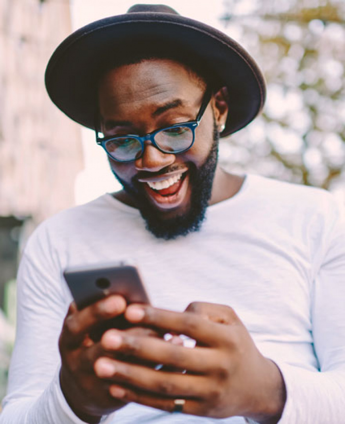 Excited man with hat beard and glasses looking at cell phone