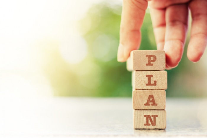 a hand placing the final block on a stack of block with letters to spell out the word plan