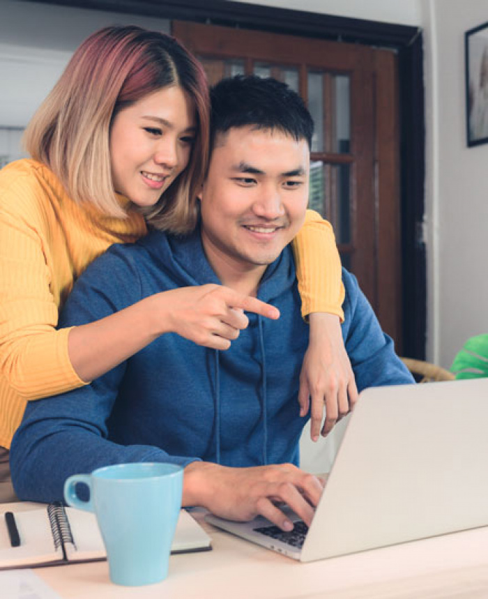 Man sitting at laptop with woman behind him who has arm over his shoulder pointing at screen