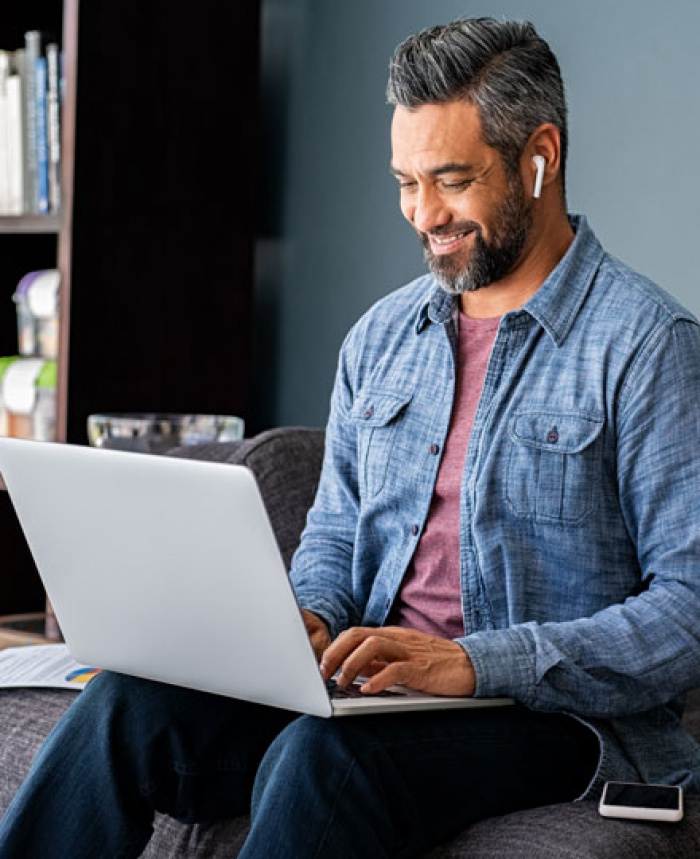 Man sitting on couch smiling and using laptop