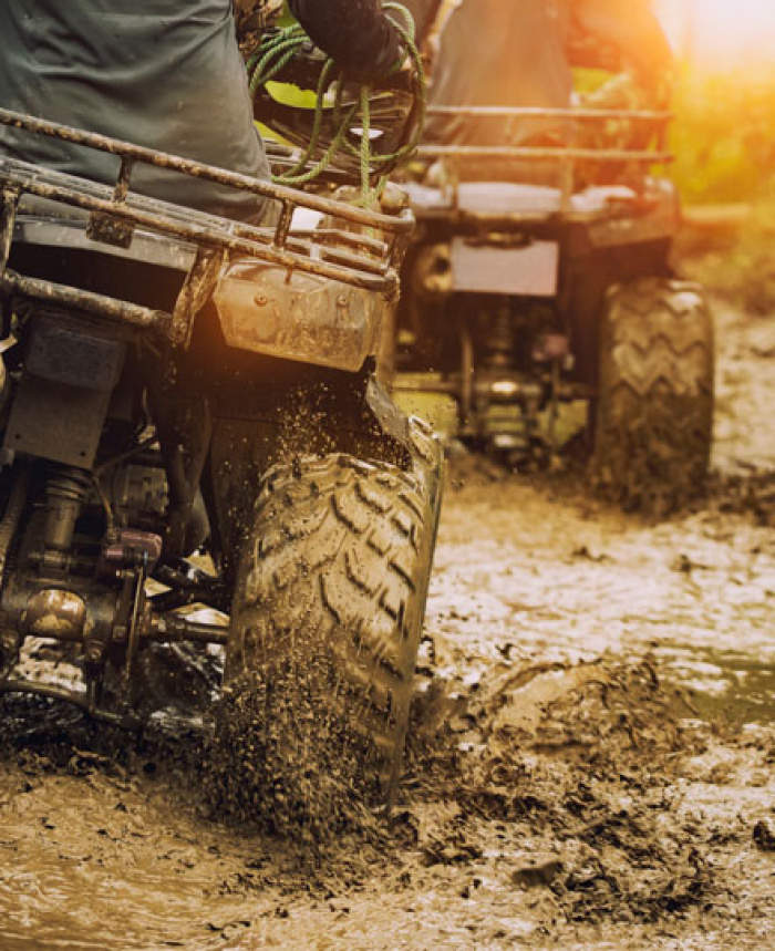 Two all terrain vehicles riding through muddy water