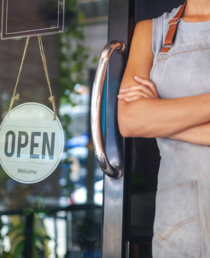 business owner with arms crossed standing by open sign