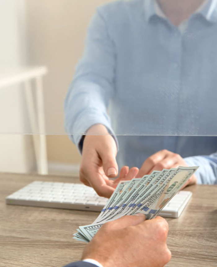 Bank teller passing one hundred dollar bills through window