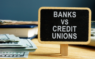 sign that reads banks vs credit unions next to a stack of 100 dollar bills